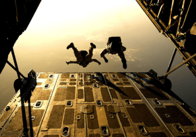 two soldiers jumping out of an airplane with sunset in background